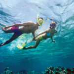 Young couple snorkelling above a shallow reef, underwater view.