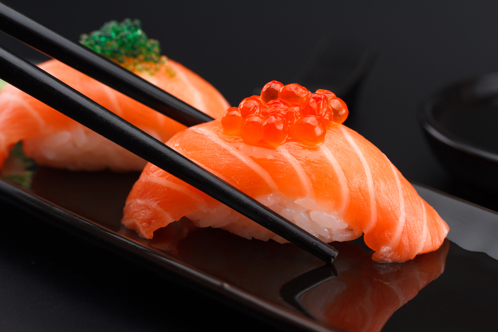 Salmon,Sushi,Nigiri,In,Chopsticks,Over,Black,Background