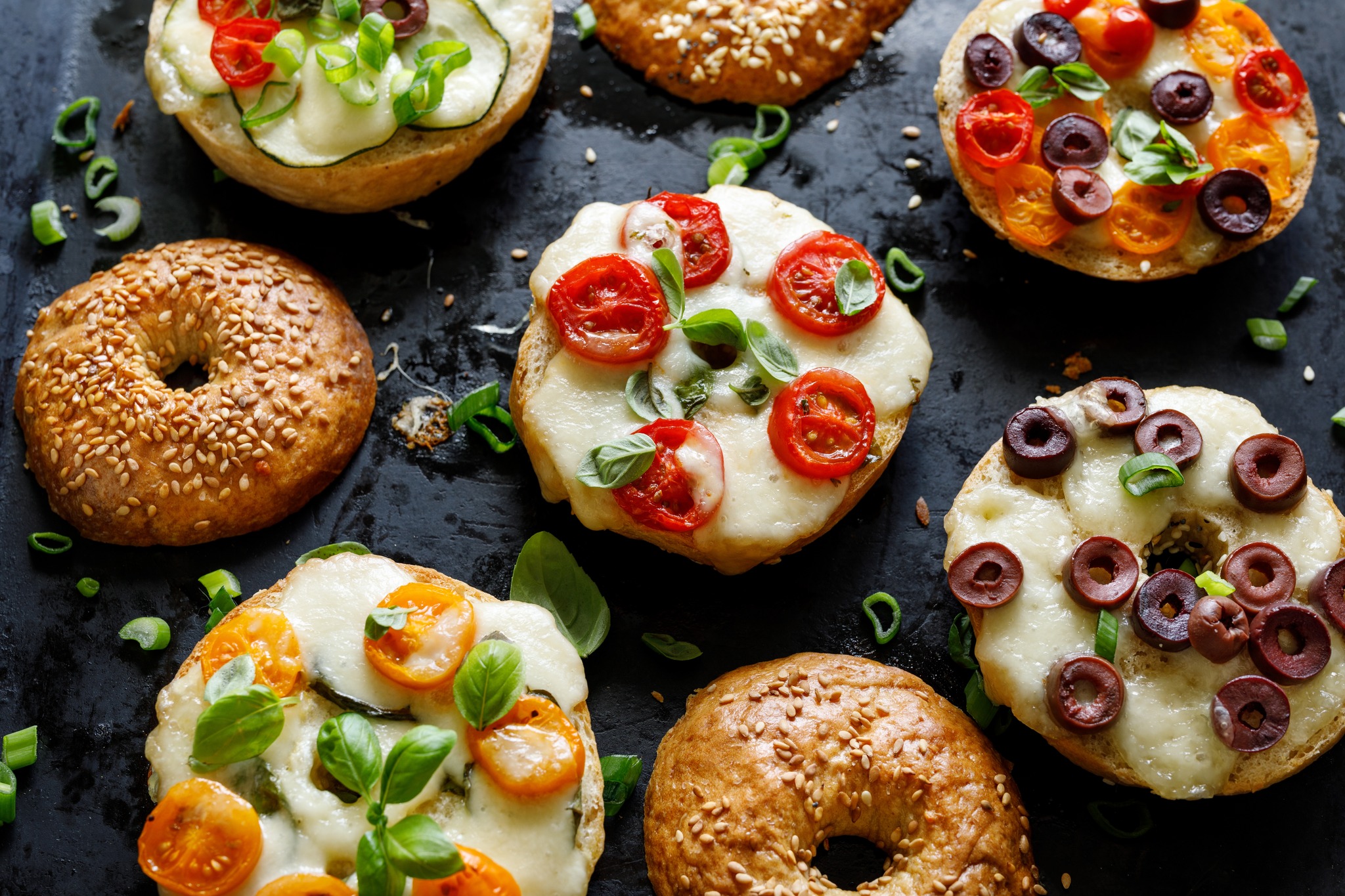 Grilled bagels  with with cherry tomatoes, olives, mozzarella cheese and herbs on a dark background,   close up view